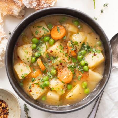 Close-up of a bowl full of easy potato stew with peas, crusty bread in the background