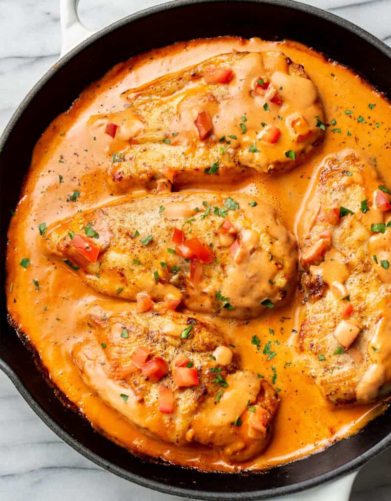 Top view of a black skillet full of chicken breasts in a creamy tomato sauce.