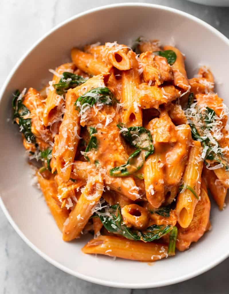 Top view of a white plate full of penne with chicken and tomato sauce.