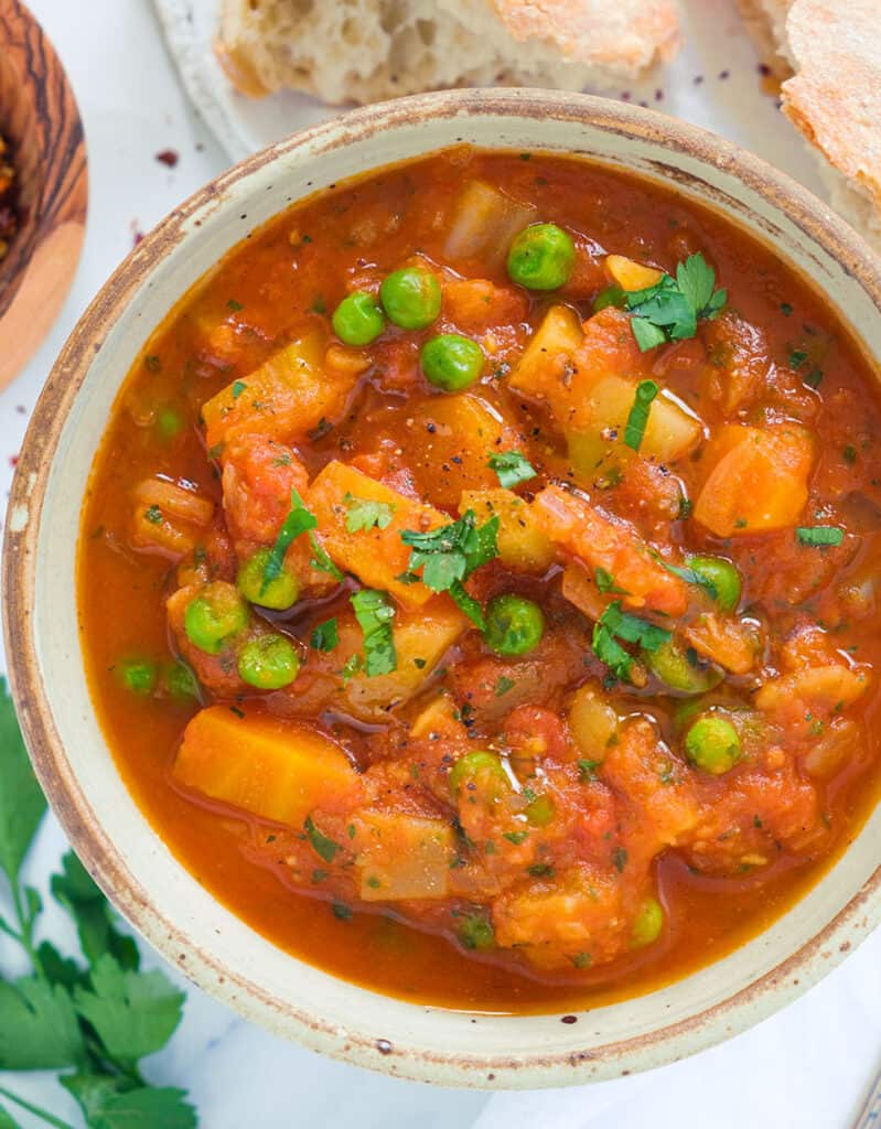 Top view of a bowl full of rich tomato stew with vegetables and peas.