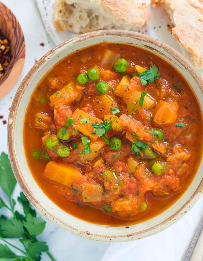 Top view of a bowl full of tomato stew with vegetables served with crusty bread.