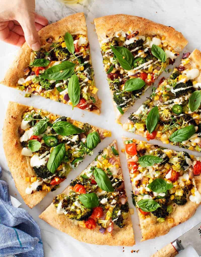 A hand grabbing a slice of a colorful vegan pizza.