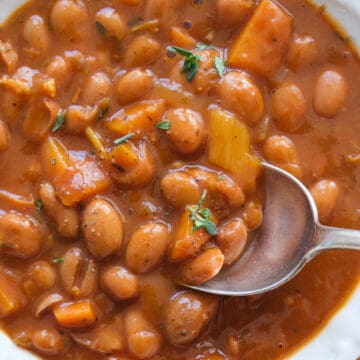 Top view of a white bowl full of bean stew cooked in a rich red wine sauce.