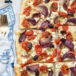 Top view of a Greek pizza with feta cheese, cherry tomatoes, olives and oregano.