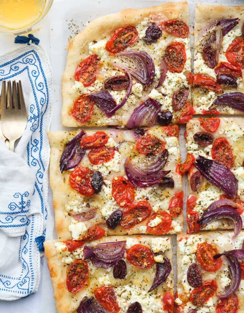 Top view of a large Greek pizza with feta cheese, red onion, cherry tomatoes, Kalamata olives and oregano.