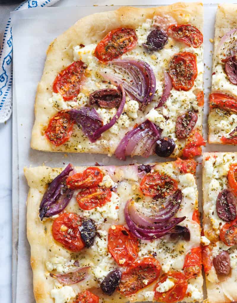 Top view of a  Greek pizza with feta cheese, roasted onion, cherry tomatoes, black olives and oregano.