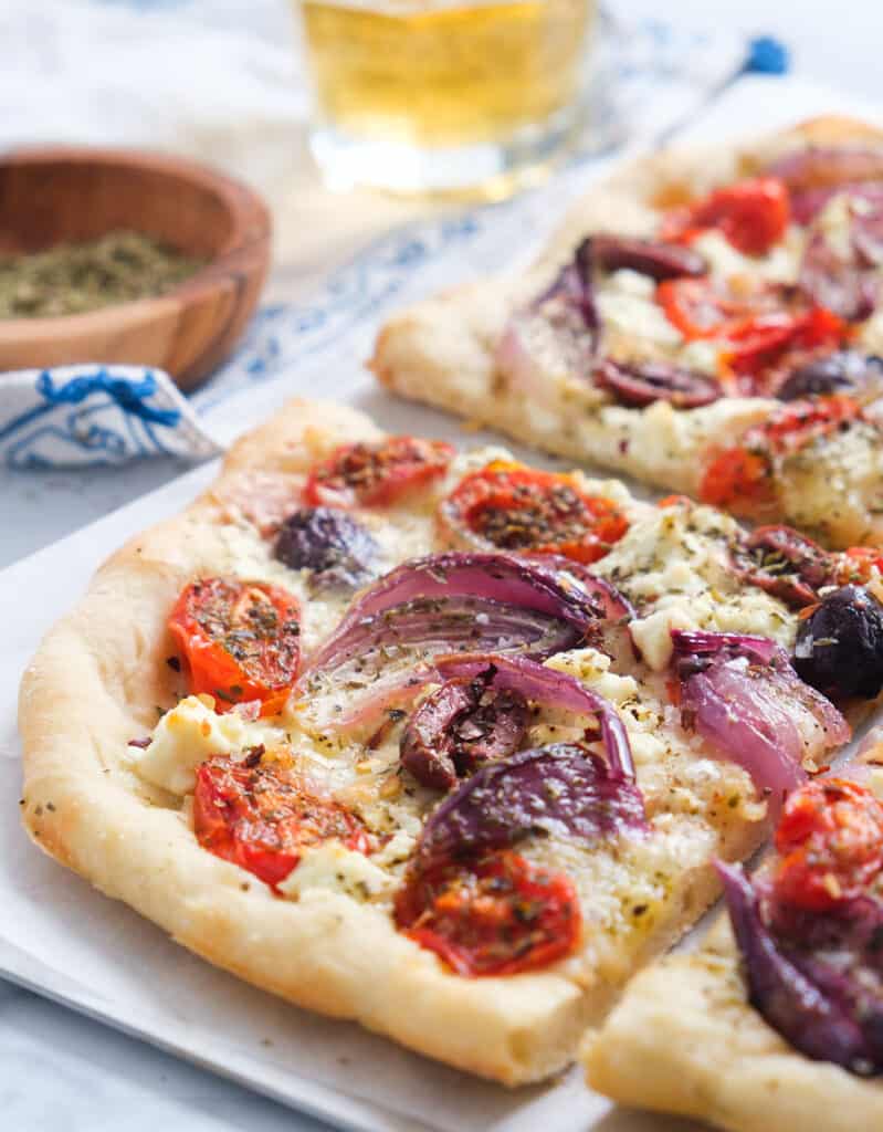 Close-up of a slice of Greek pizza with feta cheese, red onion, cherry tomatoes, olives and oregano.