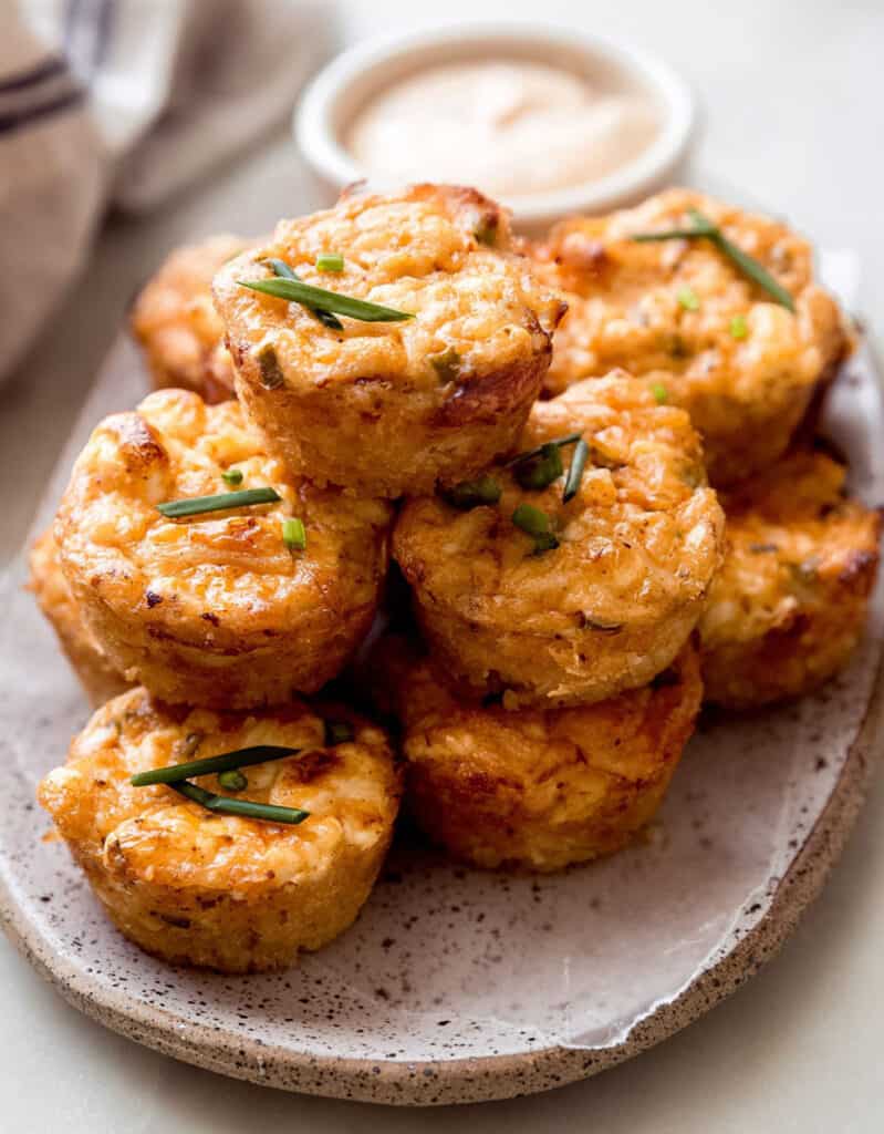 Several crab bites garnished with chives and served on a small tray with some mayo sauce on the side.