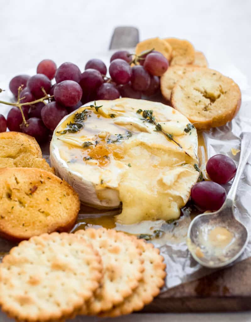 Close-up of some baked brie showing its creamy texture and surrounded by crackers and red grapes.