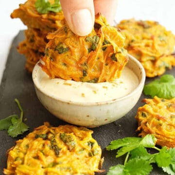 A hand dipping a carrot fritter into some hummus dip.