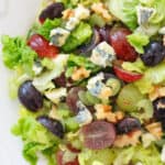Top view of a white bowl full of salad with grapes, lettuce, blue cheese and walnuts.