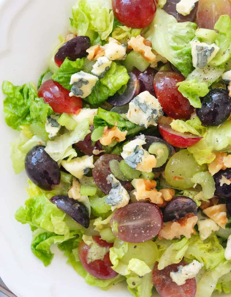 Close-up of a white bowl full of salad with grapes, lettuce, blue cheese and walnuts.