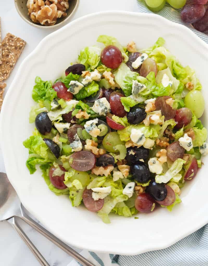 Top view of a white salad bowl full of salad with lettuce, red grapes, blue cheese and walnuts.