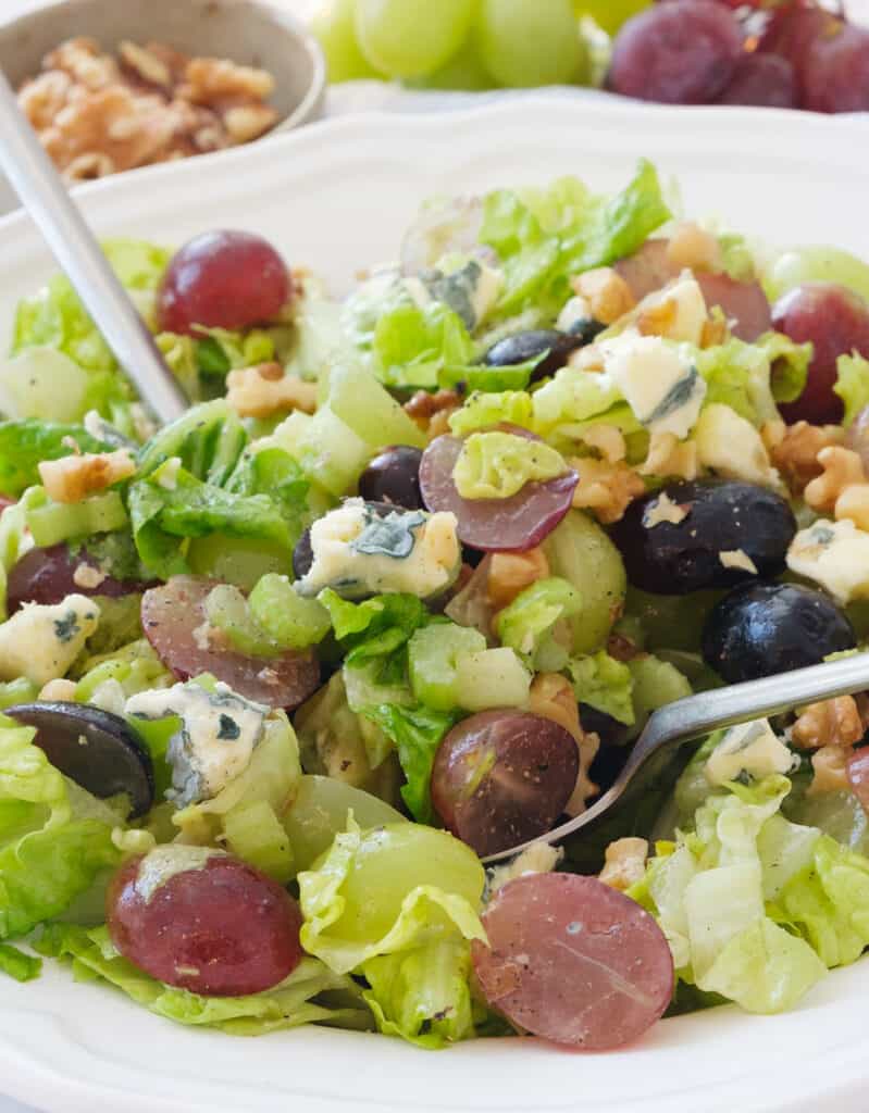 Two spoon tossing lettuce salad with grapes, blue cheese and walnuts.
