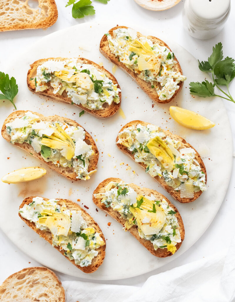 Top view of artichoke bruschetta on round marble plate.