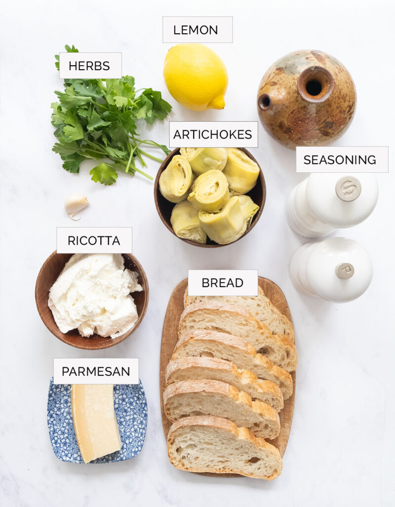 Top view of ingredients for making artichoke bruschetta on white background.