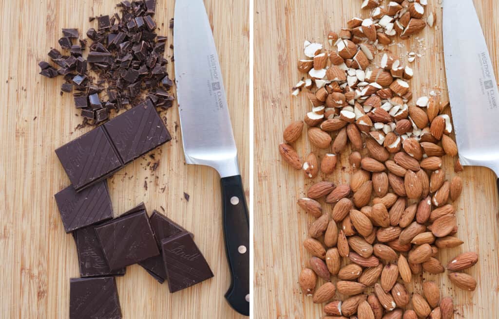 Top view of a wooden chopping board with chopped chocolate and almonds, a chef knife in the background.