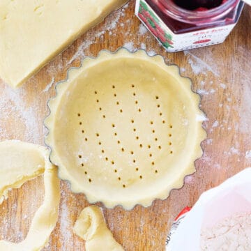 Top view of a sweet shortcrust pastry, a jar with jam in the background.