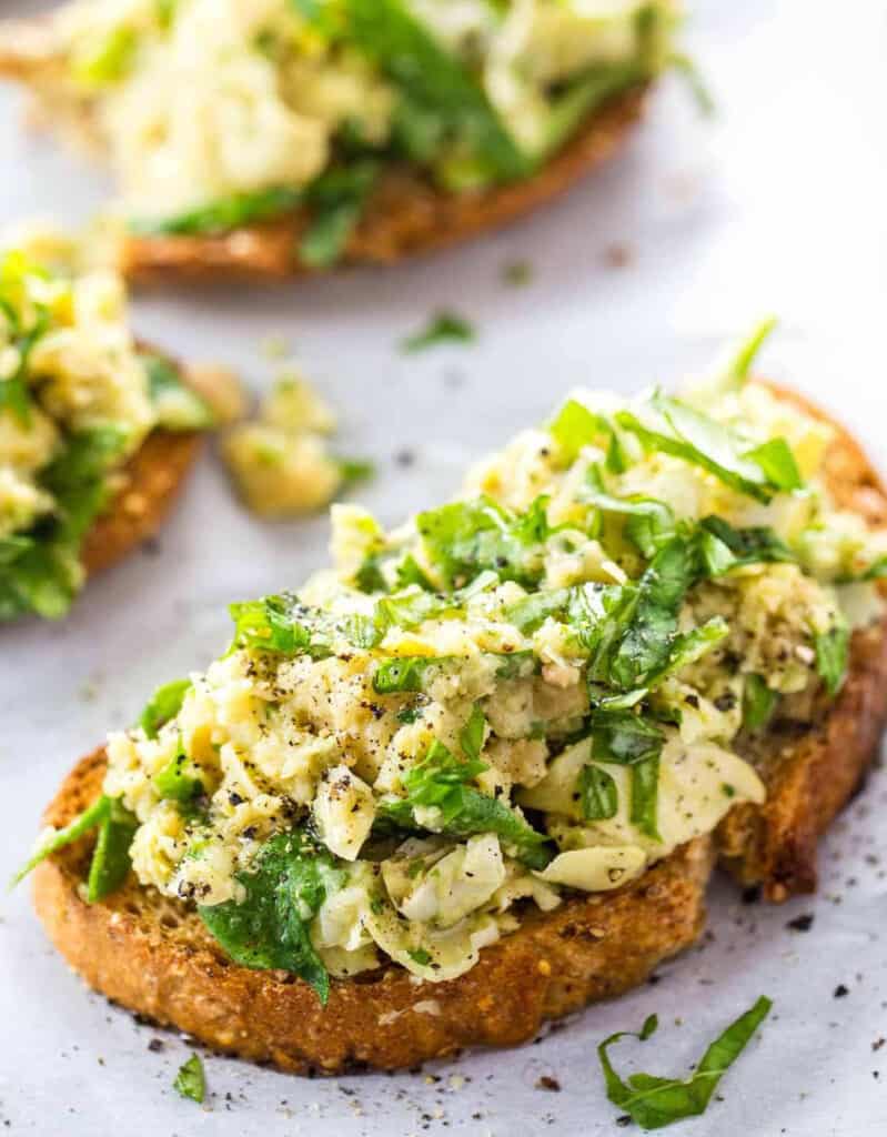 Close-up of some crispy toasts topped with artichokes and fresh herbs on a white background.