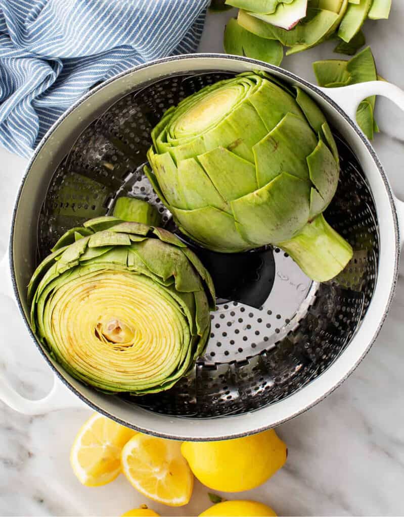 Top view of a metal colander containing two large globe artichokes before cooking.