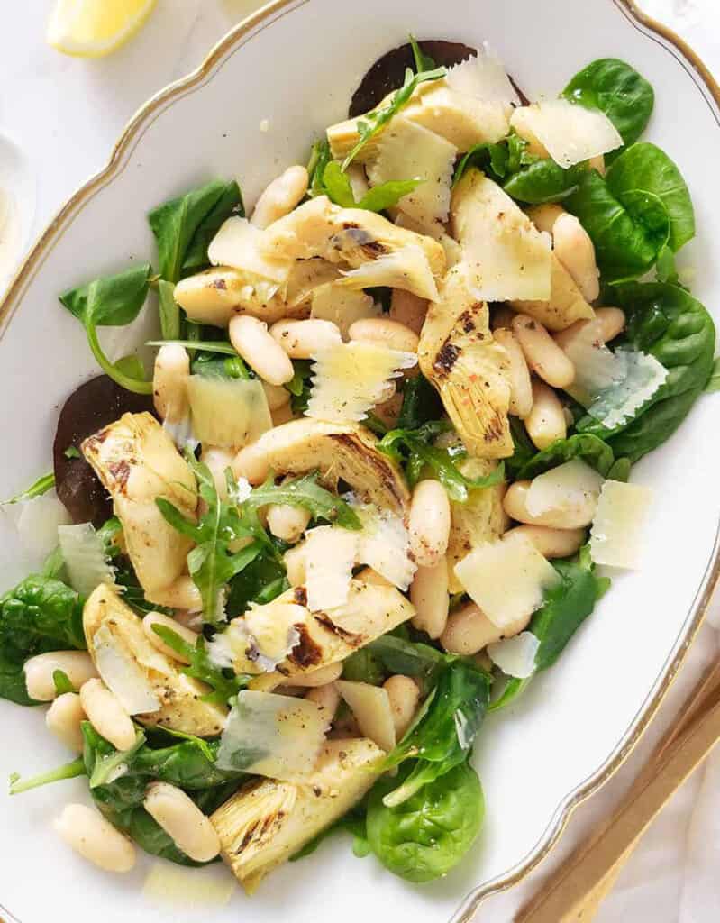 Top view of an artichoke salad with white beans and green leaves served  on a white tray.