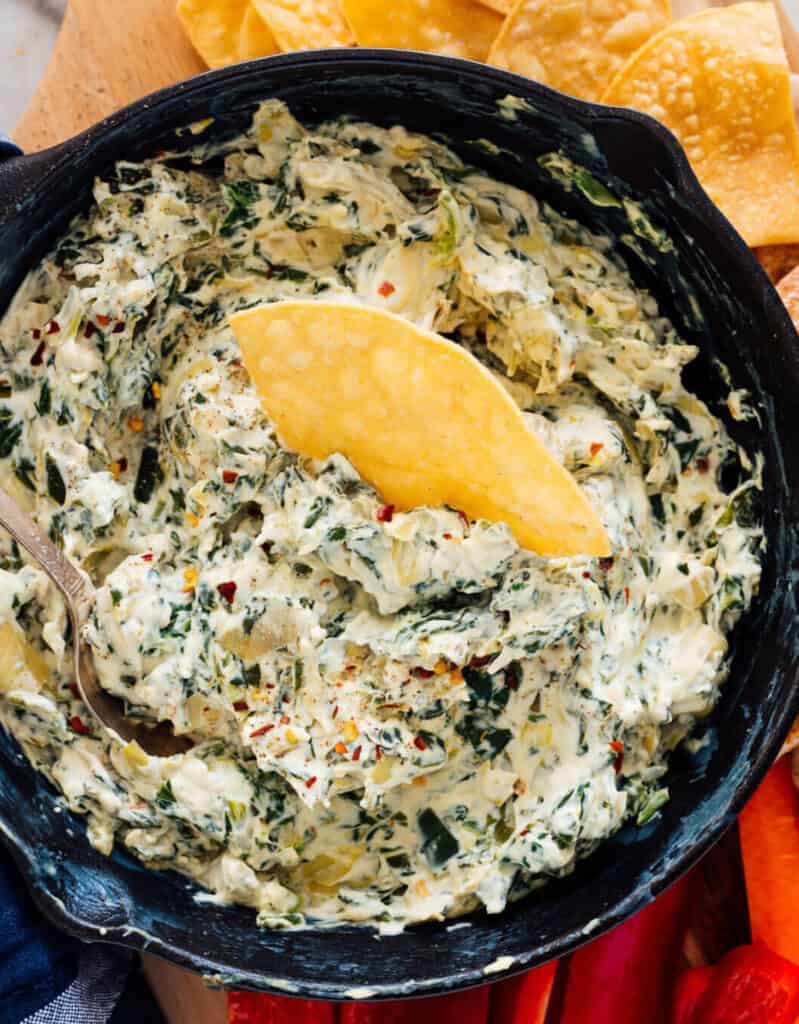 Top view of a black bowl full of artichoke dip and served with tortilla chips.