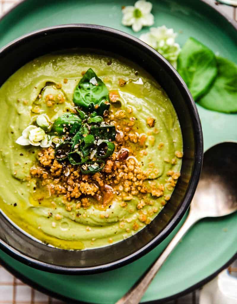 Top view of a black bowl full of green soup with artichoke and spinach.