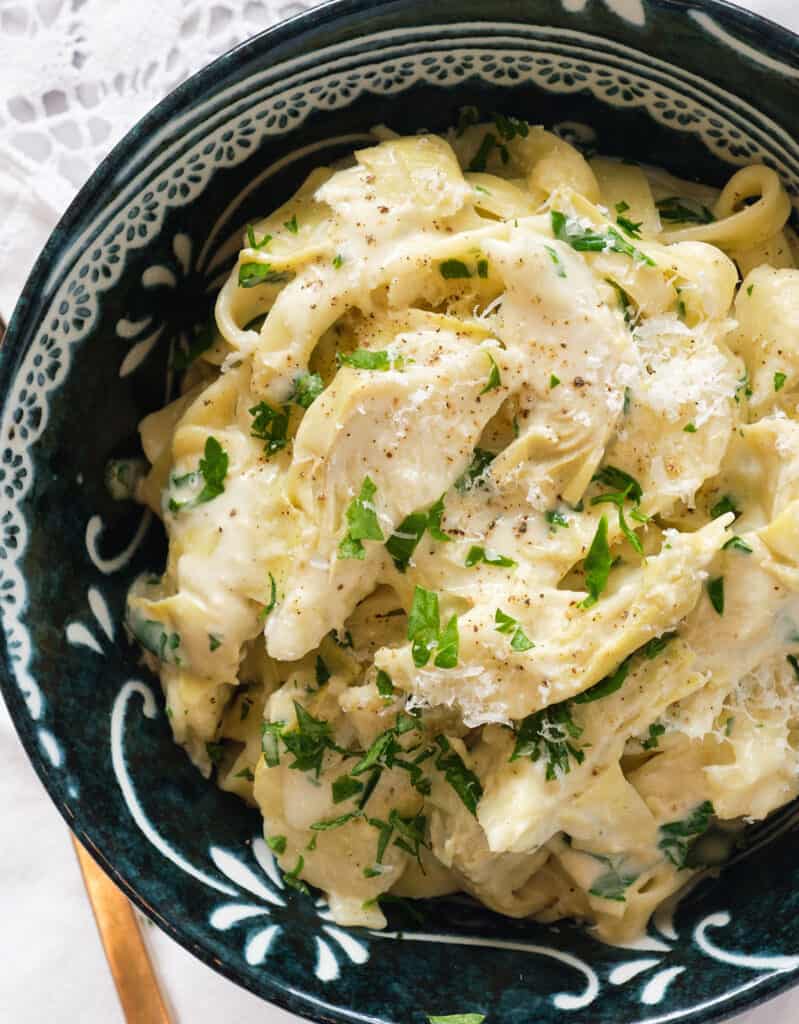 Top view of a dark bowl full of tagliatelle with artichokes and parmesan cheese.