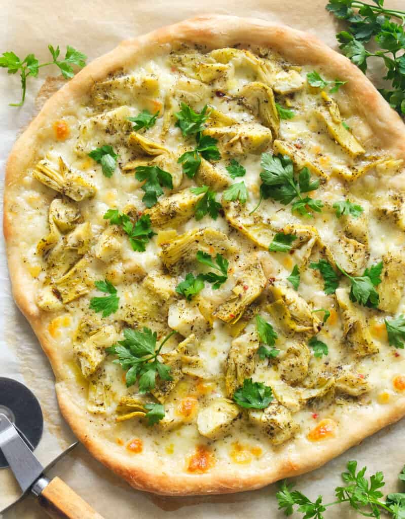 Top view of a crispy pizza with artichokes and fresh parsley.