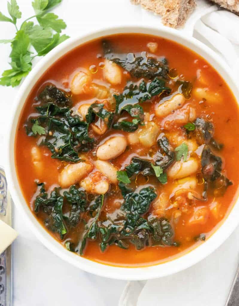 Top view of a white bowl full of white bean, kale and tomato soup.