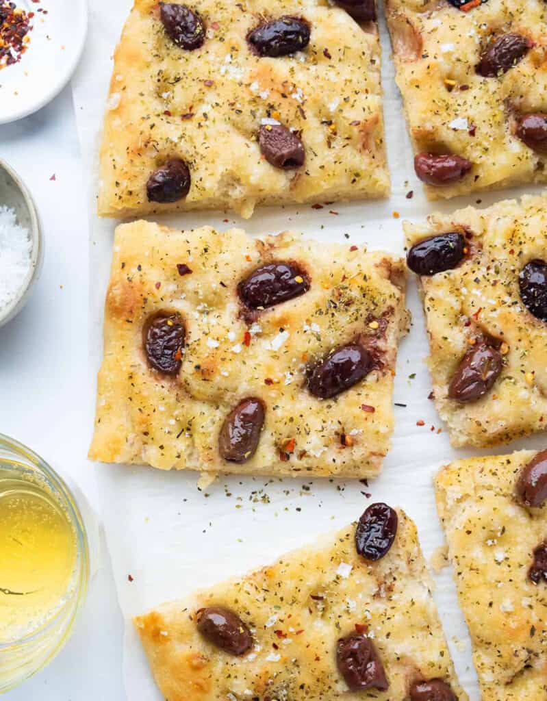 Top view of some slices of focaccia with olives and sea salt over a white background.