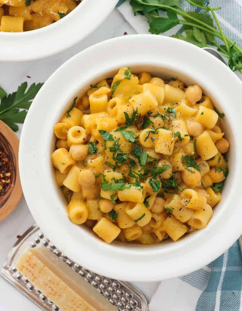 Top view of a white bowl full of ditali pasta with chickpeas garnished with fresh parsley.