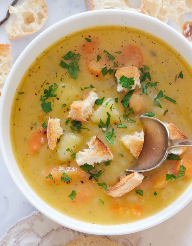 Top view of a white bowl full of carrot potato soup with croutons and fresh parsley.