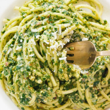 Close-up of a white plate full of yummy arugula pasta served with grated parmesan cheese.