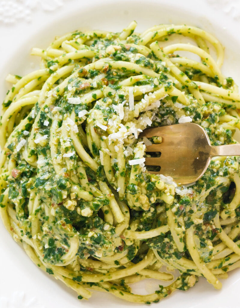 Close-up of one of the arugula recipes featuring a white plate full of arugula pasta.