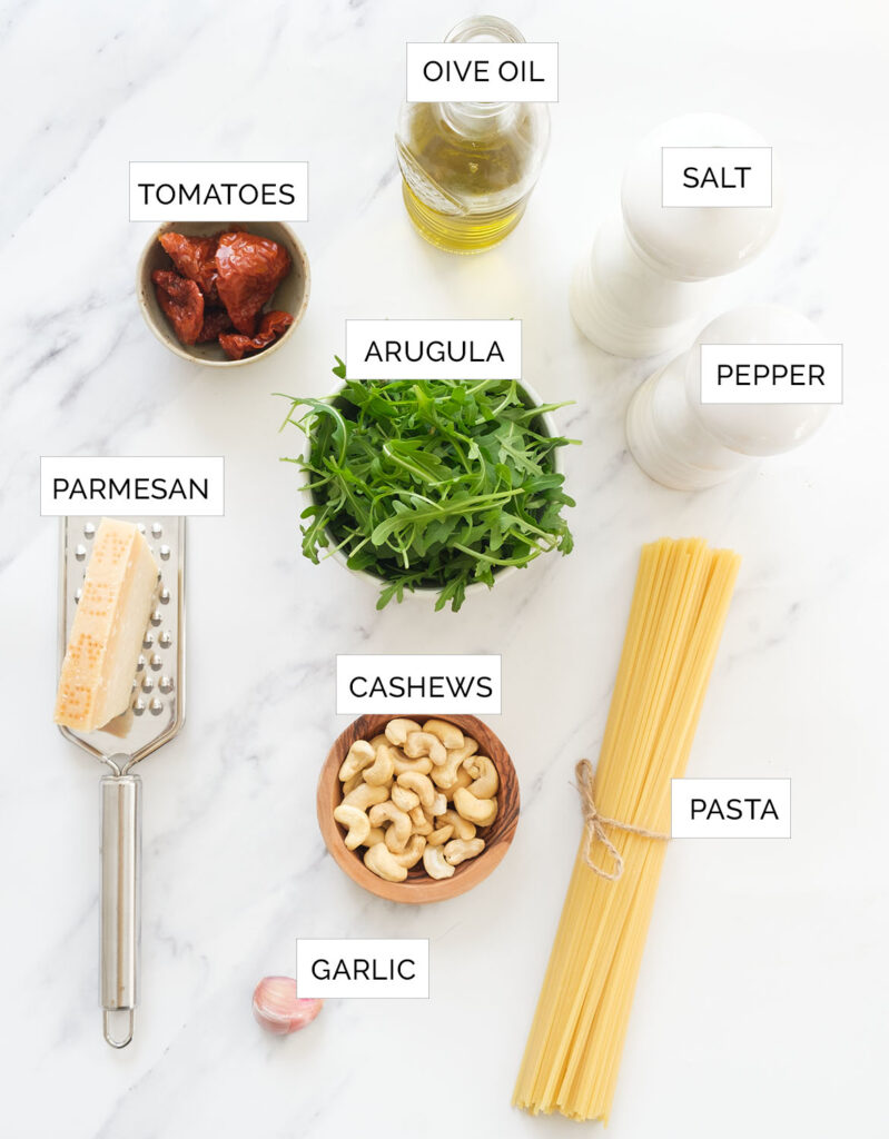 The ingredients to make arugula pasta are arranged over a white background.