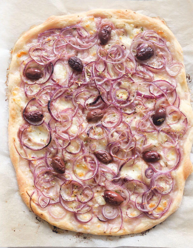 Top view of a large onion pizza with olives freshly baked.