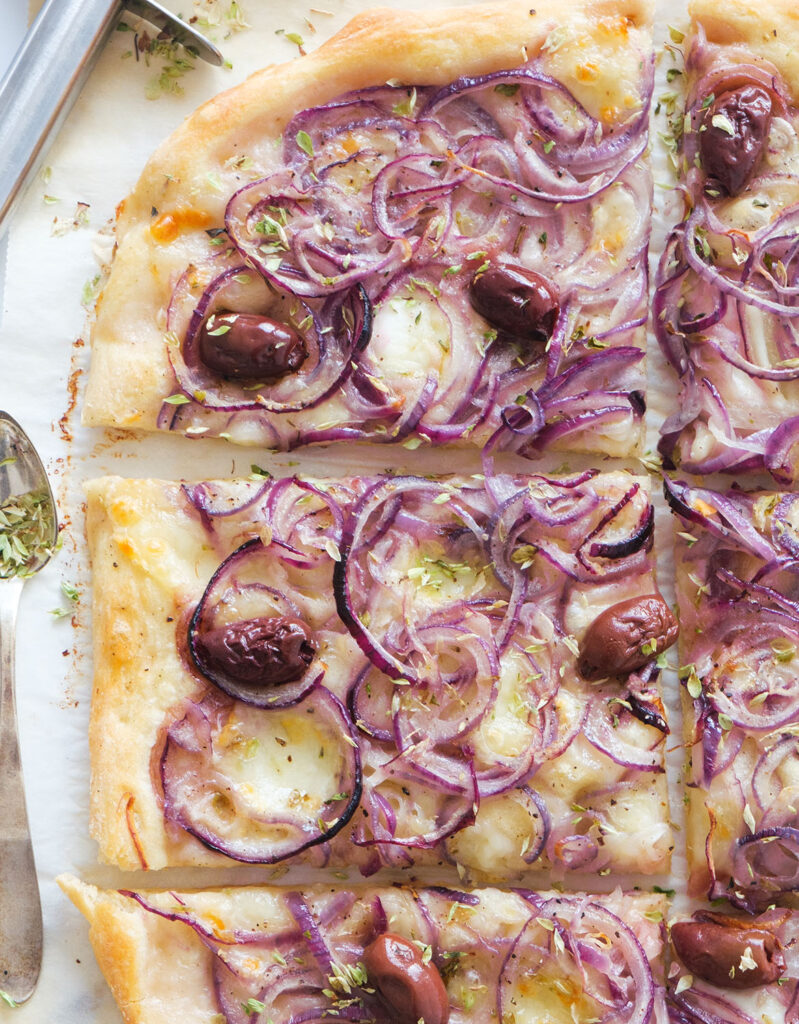 Top view of a large onion pizza with black olives cut into slices.
