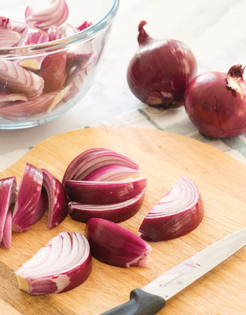 Close-up of a chopping board with red onion slices and a knife.