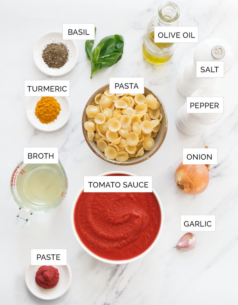 Top view of the ingredients to make the tomato soup with pasta over a white background.