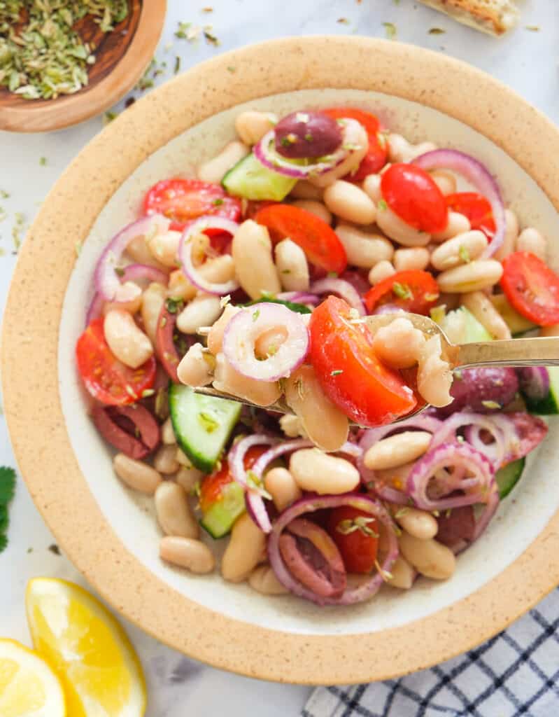 Top view of a plate full of Mediterranean bean salad with tomatoes, onions, cucumber and olives.
