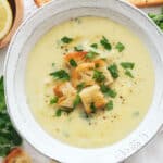 Top view of a white bowl full of creamy artichoke soup served with croutons and parsley.