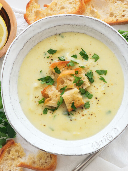 Top view of a white bowl full of creamy artichoke soup served with croutons and parsley.