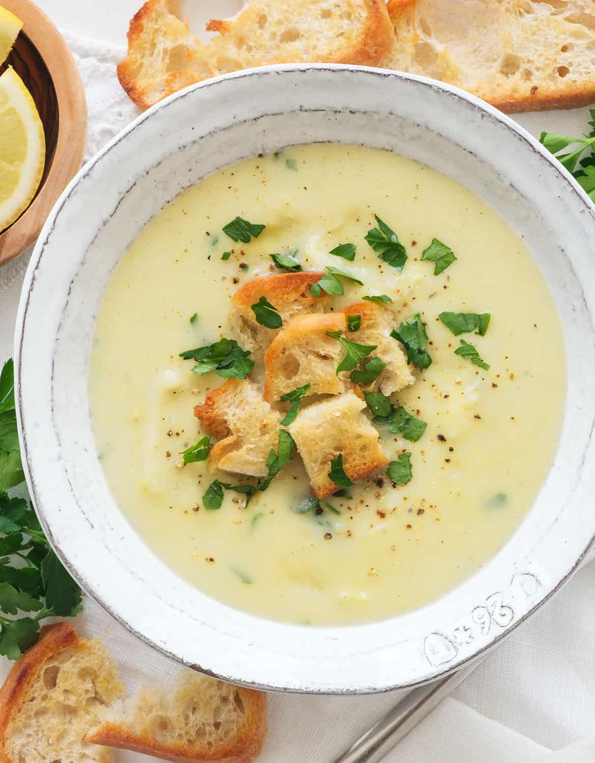 Top view of a white bowl full of creamy artichoke soup served with croutons and parsley.