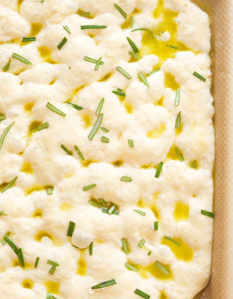 Close-up of a portion of easy focaccia with brine and rosemary before baking.