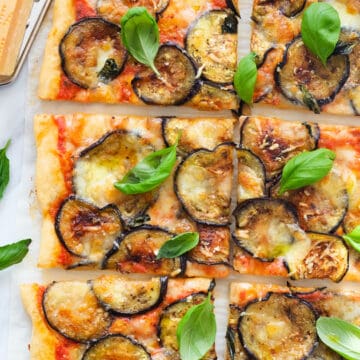 Top view of a large pizza with eggplant and fresh basil leaves cut into slices.
