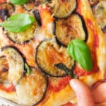 A slice of pizza with eggplant and fresh basil leaves.