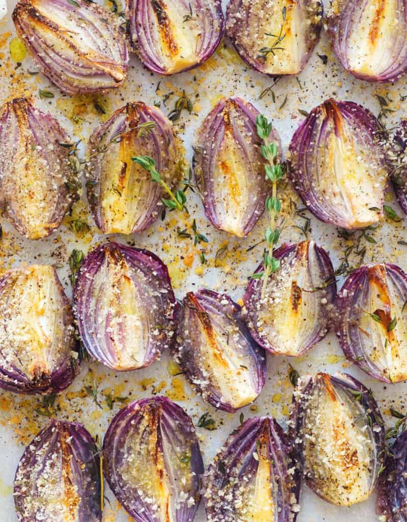 Top view of a baking tray full of roasted onions with thyme and breadcrumbs.