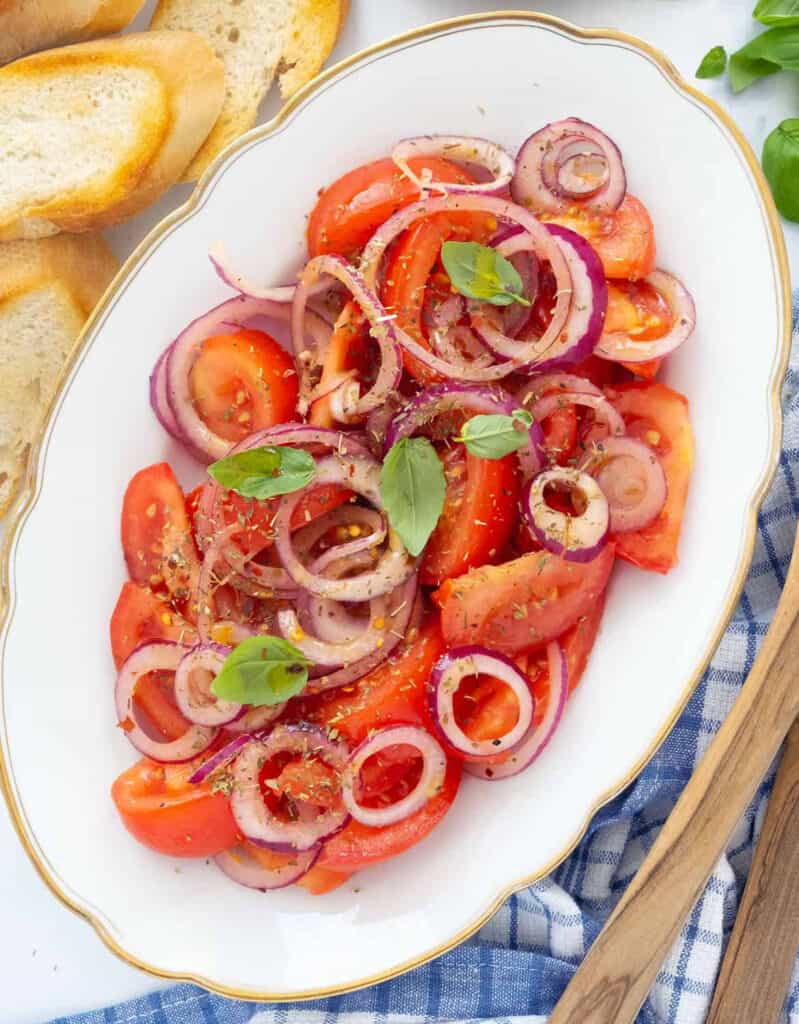 Top view of a white serving tray full of tomato and onion salad served with crusty bread.
