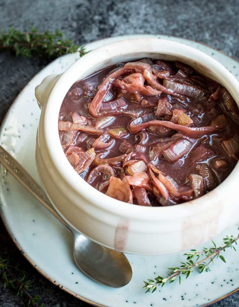 Close-up of a white bowl full of caramelized onion with red wine gravy.